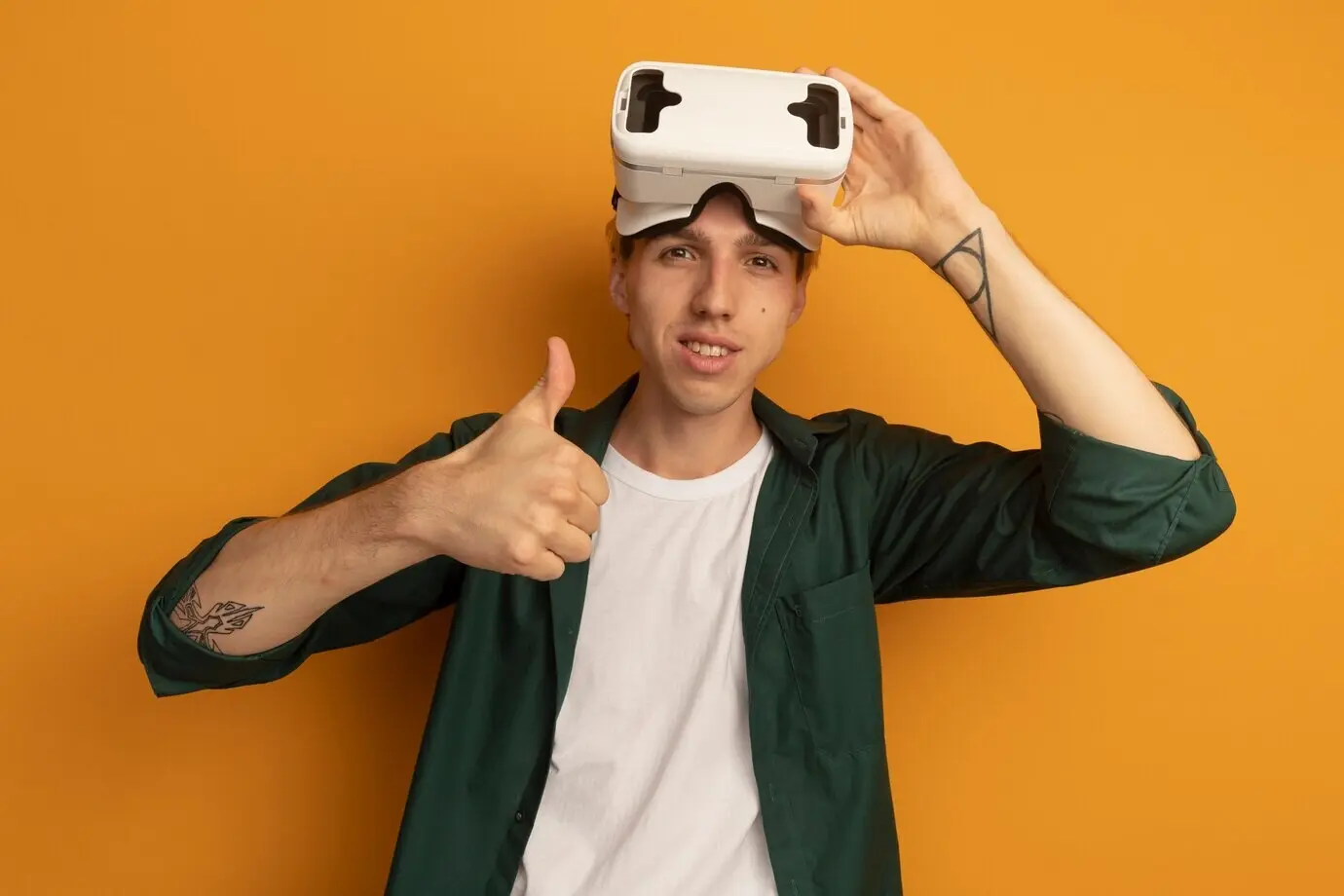 Довольный молодой светловолосый парень в зелёной футболке и VR-гарнитуре, показывающий большой палец вверх.